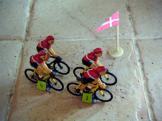Quatre équipes de cyclistes miniatures, chacune avec son fanion de couleur